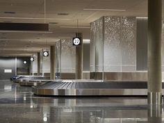 an empty airport terminal with luggage carousels in the foreground and clock on the wall