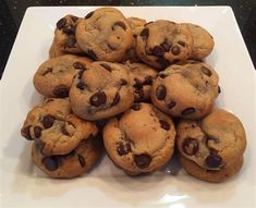 a white plate topped with lots of chocolate chip cookies on top of a countertop