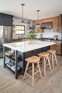 a large kitchen with wooden stools next to an island and stainless steel refrigerator freezer