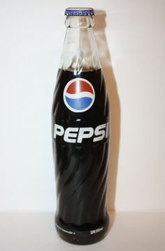 a bottle of pepsi soda sitting on top of a table next to a white wall