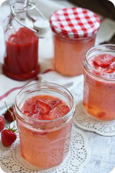 two jars filled with strawberry jam sitting on top of a table next to strawberries