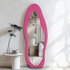 there is a pink mirror on the wall next to a white table with a vase