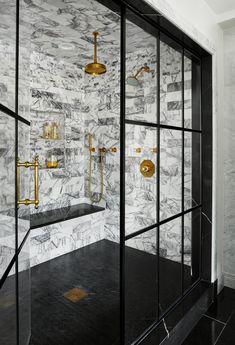 a bathroom with black and white marble walls, gold fixtures and glass shower enclosures