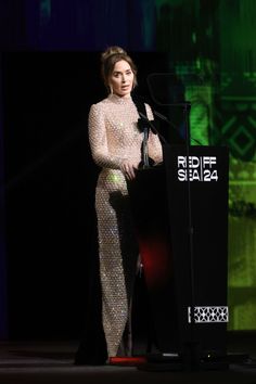 a woman standing at a podium in front of a microphone and wearing a white dress