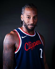 a man with tattoos on his arm wearing a blue jersey and standing in front of a black background