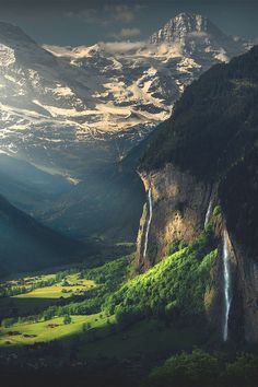 the mountains are covered in snow and green grass, with a waterfall running down them