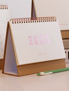 a desk calendar sitting on top of a table next to a green pen and pencil