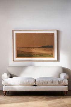 a white couch sitting under a painting in a living room next to a wooden floor