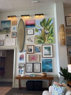 a living room filled with lots of pictures and paintings on the wall above a wooden table