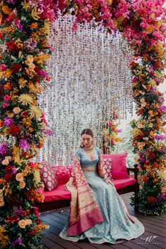 a woman sitting on top of a red couch under a flower covered arbor with pink and yellow flowers