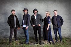 five people standing in front of a wall with one person wearing a cowboy hat and the other looking at the camera