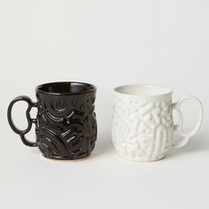 two black and white coffee mugs sitting next to each other on a white surface