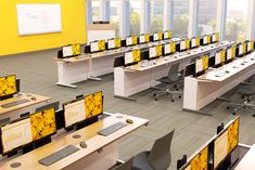 rows of desks with computers on them in an office building or conference room that has yellow walls and carpeted flooring