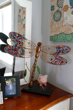 a dragonfly sculpture sitting on top of a wooden table next to a framed photo