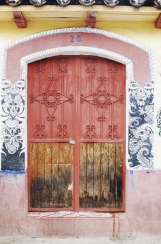 an old red door with ornate designs on the side of a pink and yellow building