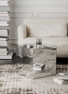 a mirrored table sitting on top of a rug next to a white couch and books