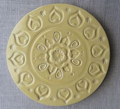 a yellow plate with designs on it sitting on a gray tableclothed surface,