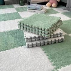 a green and white rug on the floor next to a teddy bear, two books and a stuffed animal