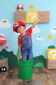 a young boy in overalls and a red hat standing on top of a green trash can