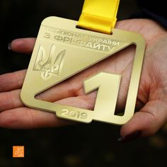 a person holding a gold medal in their left hand with a yellow ribbon around it