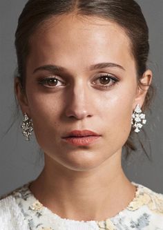 a close up of a person wearing earrings and looking at the camera with a serious look on her face