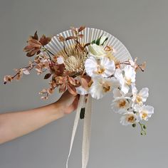 a hand holding a white fan with flowers on it and ribbon tied around the handle