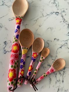 six wooden spoons are lined up on a marble counter top, with floral designs