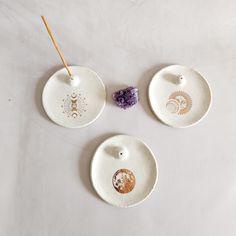 three white plates with designs on them sitting next to two purple flowers and one orange flower