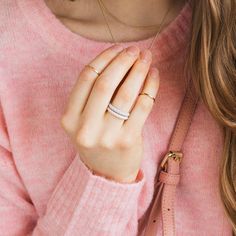 a woman wearing a pink sweater holds her hand up to her chest and wears a diamond ring