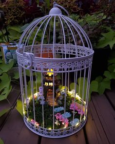 a white birdcage filled with lots of flowers and lights sitting on top of a wooden table