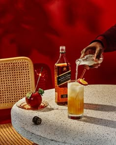 a person pours an apple cider into a glass on a table with two chairs