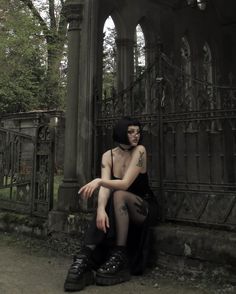 a woman sitting on the ground in front of an iron gate