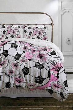 a bed with pink flowers and soccer balls on the comforter, next to a white wall