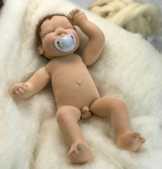 a baby doll with a pacifier on it's face laying on a white blanket