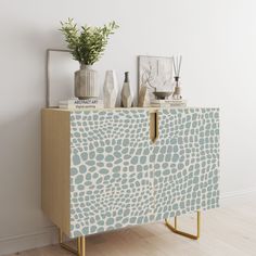 a sideboard with vases and plants on top in a white walled room next to a wall