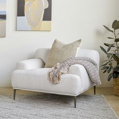 a living room with a white chair and paintings on the wall above it, along with a rug