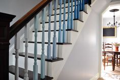 an open door leading to a dining room and living room area with white walls, wood stairs and blue railings