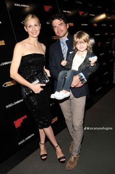 a man, woman and child standing in front of a red carpeted wall at an event