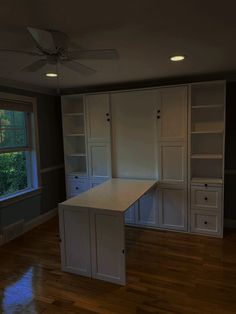 an empty room with white cabinets and wood floors in the middle of it is lit by a ceiling fan