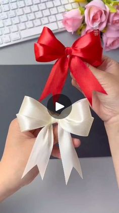 someone is holding a red and white bow in front of a computer desk with flowers