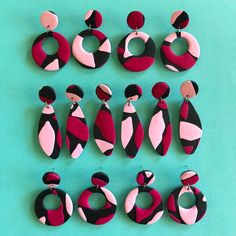 several pairs of earrings are arranged on a green surface, including pink and black shapes