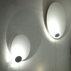 two circular lights hanging from the ceiling above a bed in a room with white walls