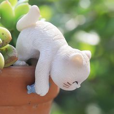 a white cat figurine sitting on top of a potted plant