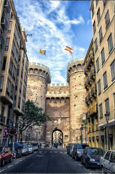 the entrance to an old castle with flags flying in the air above it and cars parked on the street below