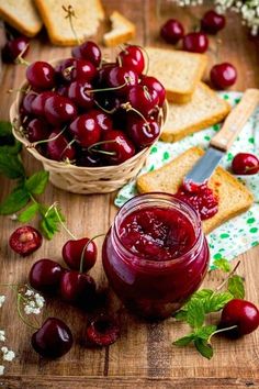 cherries and bread on a cutting board next to a jar of jam with fresh cherries in the background