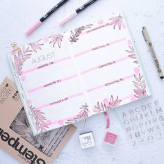 an open planner with pink flowers on it next to some markers and pencils, along with other items