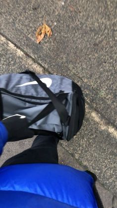 a person with their feet on the ground next to a blue bag and a leaf