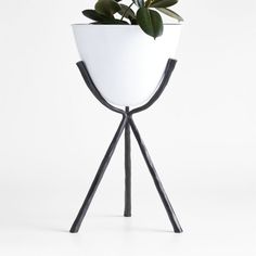 a white planter sitting on top of a wooden stand with two black legs and a green plant in it