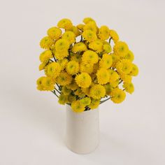 a white vase filled with yellow flowers on top of a table