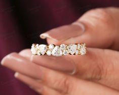 a woman's hand holding a gold ring with five stones on it and two fingers